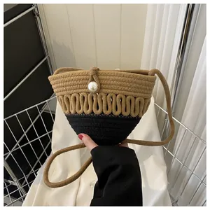 Detail of woven straw crossbody bag with contrast stitching and oversized pearl bead
