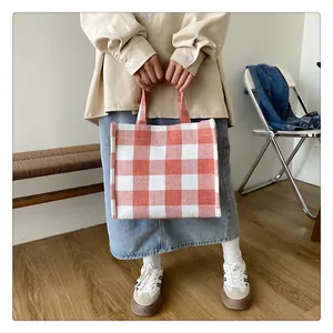 Détail d'un sac cabas rectangulaire en toile à carreaux orange et blanc tenu par un mannequin