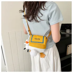 Detail of yellow canvas crossbody bag featuring a plush duck doll and adjustable strap