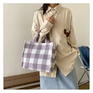 Gros plan d'un sac cabas à carreaux violets et blancs tenu par un mannequin en chemise