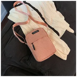 Close-up of pink corduroy crossbody bag with adjustable strap and brand nameplate