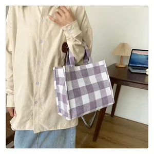 Détail d'un sac cabas à carreaux violets et blancs tenu par un mannequin en intérieur