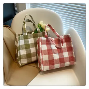 Détail de sacs fourre-tout en toile à carreaux verts et rouges posés sur une chaise blanche