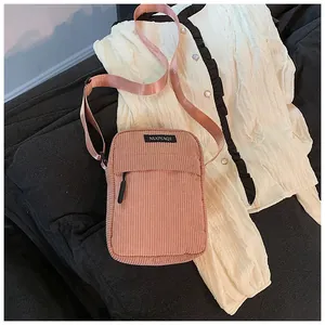 Detail of pink corduroy crossbody bag featuring a front zipper pocket and fabric logo tag