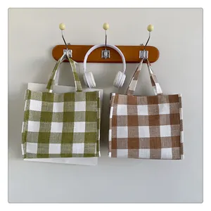 Détail de sacs cabas en toile à carreaux vert et beige suspendus à un crochet mural en bois