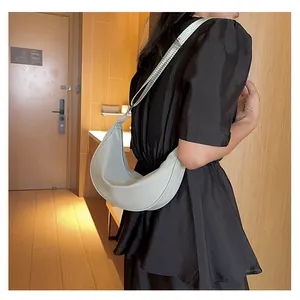 Dettaglio di una borsa a mezzaluna grigia indossata da una modella in un interno casual