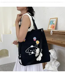 Détail d'un cabas noir en toile avec imprimé cartoon, pendentif ours et badges mignons