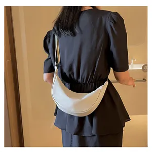 Dettaglio di una borsa a tracolla beige a mezzaluna indossata su un vestito nero elegante