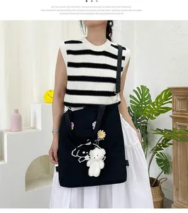 Détail d'un sac cabas en toile noire avec broderie de personnage et pendentif ours