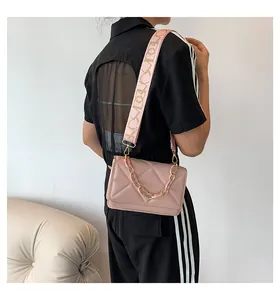 Detail of pink crossbody bag with acrylic chain and quilted pattern on light sofa