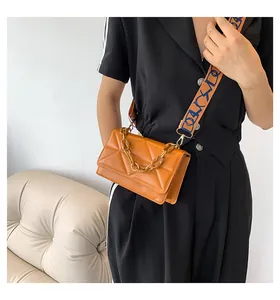 Close-up of orange quilted crossbody bag with chunky acrylic chain and patterned wide strap