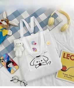 Détail d'un sac en toile blanc avec motif chien, ours en peluche et broches déco