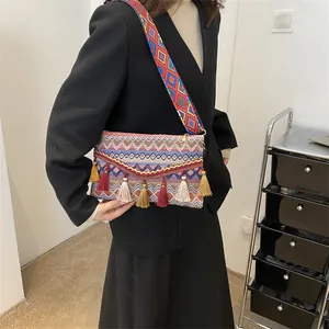Ethnic woven crossbody bag with geometric patterns and colorful tassels on wide strap