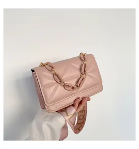 Close-up of pink quilted crossbody bag featuring a wide woven strap and acrylic chain detail