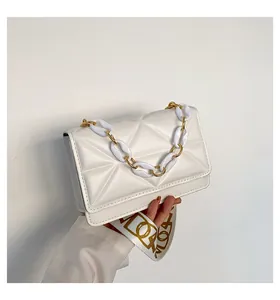 Detail of white leather shoulder bag featuring 3D triangle quilting and acrylic chain strap