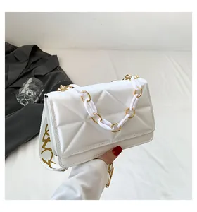 Close-up of white quilted handbag with chunky gold acrylic chain and wide patterned strap