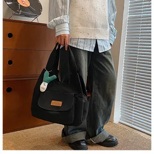 Detail of black canvas tote bag with front pocket and green plush doll charm attached