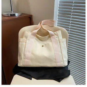 Detail of canvas tote bag showing side pockets and pink shoulder straps on white chair