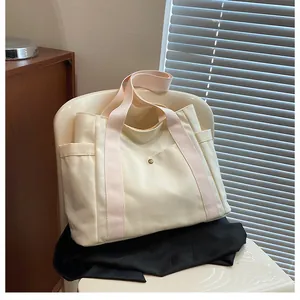 Close-up of large canvas tote bag with pink straps and pockets on a white chair