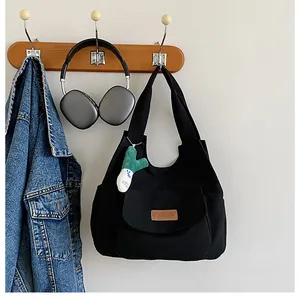Detail view of black canvas tote bag with brown leather label and plush charm on wooden hook