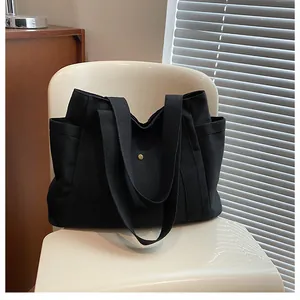 Detail of black canvas tote bag showing dual handles and secure metal snap button closure