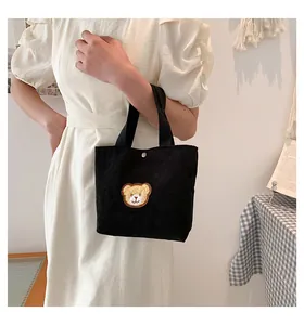 Close-up of black corduroy mini handbag featuring a cute plush bear patch and metal snap