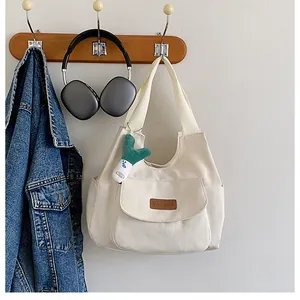 Detail of canvas tote with front pocket, fashion label and green plush charm