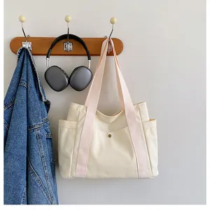 Detail view of beige canvas tote bag showing side pockets and metal snap closure