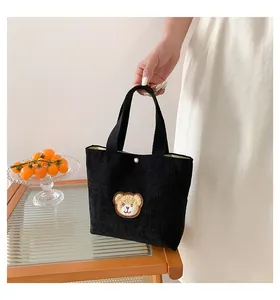 Close-up of black corduroy handbag featuring a cute bear embroidery and snap closure