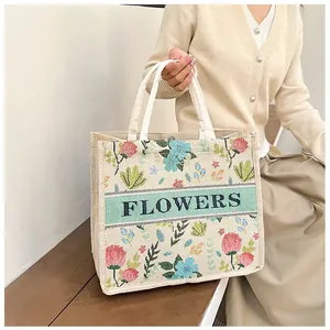 Detailed embroidery of pink flowers and FLOWERS text on a beige linen tote bag