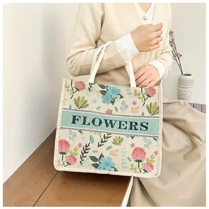 Detail of embroidered floral patterns on beige linen tote bag with FLOWERS text
