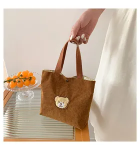 Close-up of brown corduroy handbag featuring a cute cartoon bear patch and metal button
