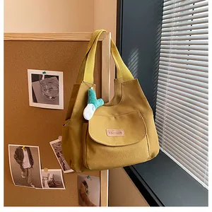 Detail of yellow canvas tote bag with side pocket, fashion label and plush charm