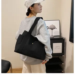 Close-up of black canvas tote bag with side pocket shown on shoulder in a casual setting