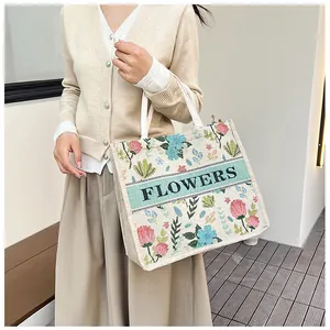 Detailed view of cream embroidered floral tote bag held by a model in casual attire