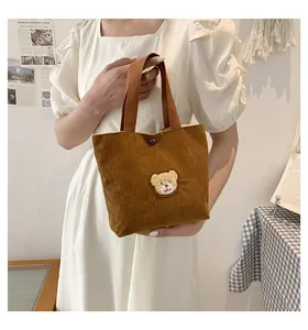 Detail of brown corduroy tote bag featuring a cute bear patch and metal snap button