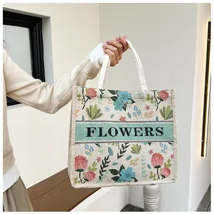 Detail shot of a beige woven tote bag featuring floral embroidery and a FLOWERS text label
