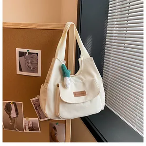 Detail of canvas tote bag with fashion label pocket and plush green charm accessory