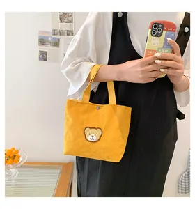 Detail of yellow corduroy tote bag featuring a cute cartoon bear patch and snap closure