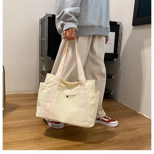 Detail of beige canvas tote bag showing front snap pocket and pink ribbon handles