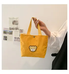 Detail of yellow corduroy tote bag with brown bear patch and metal snap button closure