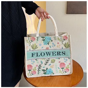Detailed close-up of ethnic floral embroidery and Flowers logo on linen tote bag