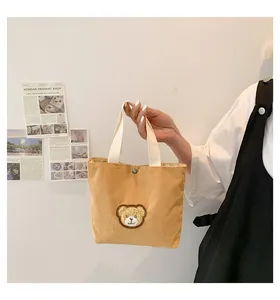 Detail of yellow corduroy handbag showing bear embroidery and soft textured fabric