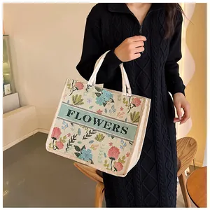 Detail of embroidered floral canvas tote bag with FLOWERS text held by a model