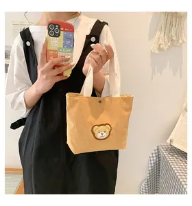 Close-up of yellow corduroy handbag with cute plush bear patch and durable web handles