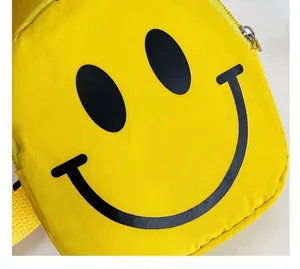 Détail d'un sac bandoulière jaune en nylon avec motif smiley noir et fermeture éclair