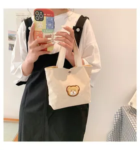 Detailed close-up of corduroy tote bag with brown plush bear patch and metal snap button
