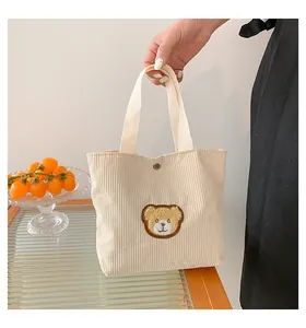 Detail of beige corduroy mini tote bag featuring brown teddy bear embroidery and snap closure