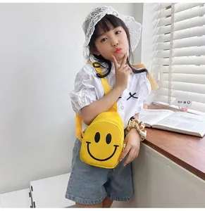 Détail d'un petit sac bandoulière jaune en toile pour enfants avec un motif smiley noir iconique