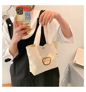 Detail of cream corduroy tote bag featuring a cute teddy bear embroidery and snap button